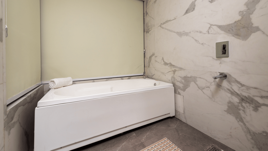 A bathroom with a bathtub, wall tiles, and fittings arranged indoors at DLS Hotels Amritsar.