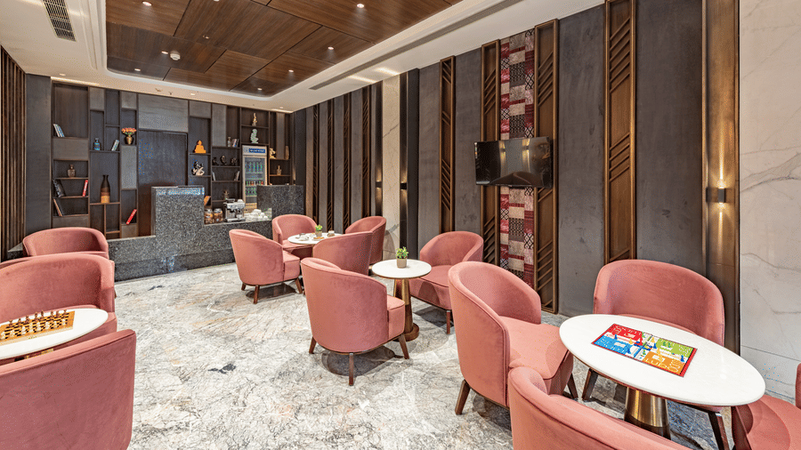 A cafe at DLS Hotels Amritsar, with multiple chairs, tables, ceiling lights, wooden panels, and decor arranged for seating.