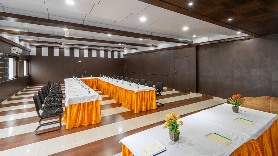A conference room with a long table, chairs, and decorative flowers on the table. The room features wooden paneling and a checkered floor - DLS Meghavan Resort, Dharamshala