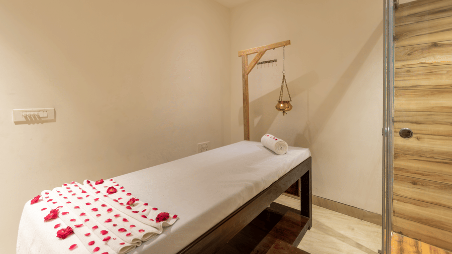 image of spa with a bed decorated with rose petals and a Shirodhara vessel at DLS The Classio