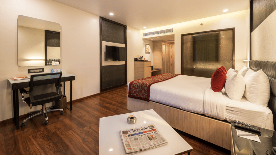Club Room at The Citrine, Bangalore, featuring a king bed with red pillows, work desk with mirror, wall-mounted TV, and dark wood flooring.