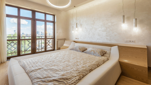 An image of a room with decorative lighting, a queen size bed, and an expansive glass door leading to the balcony