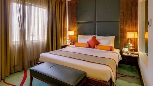 Suite at Pride Premier Chennai featuring a plush bed and a diwan placed at its foot next to a window covered with curtains