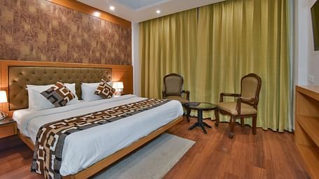 A large bed placed next to two chairs in the Deluxe Room at DLS Highland Resort and Spa, Mussoorie.