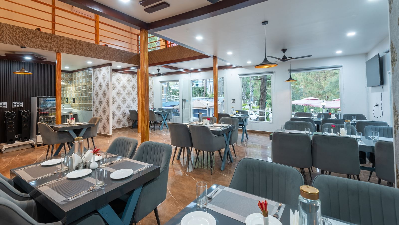 Contemporary restaurant dining area with neatly set tables, cushioned chairs, ceiling fans, and large windows providing natural light - DLS Nature Trinket Resort, Dalhousie.
