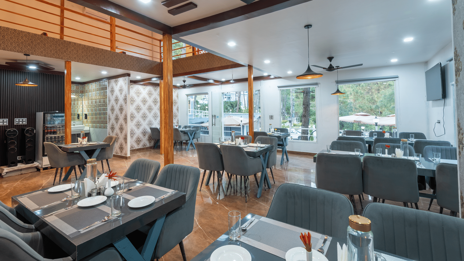A contemporary restaurant area with neatly set tables, cushioned chairs, ceiling fans, and large windows providing natural light - DLS Nature Trinket Resort, Dalhousie