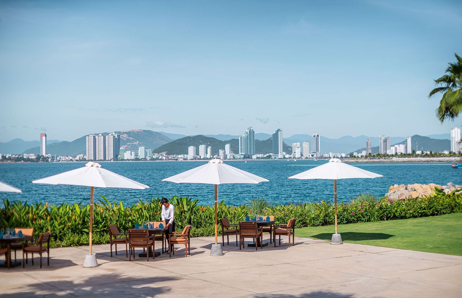 An image of a riverside with huge umbrellas and chairs underneath  - Alibu Resorts Nha Trang