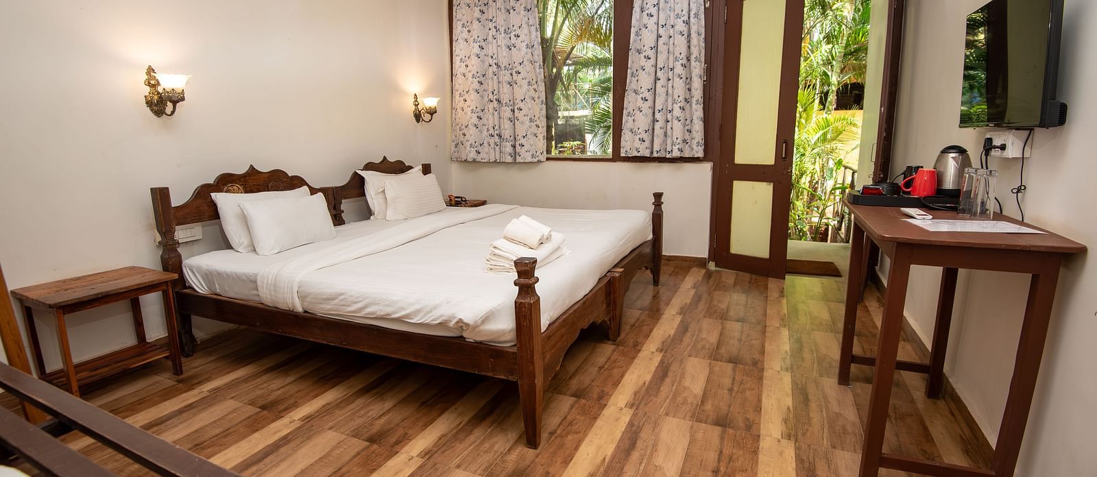 Bright guest room with a double bed, wooden flooring, a flat-screen TV, and natural light streaming in at De Soul Santé, Morjim.