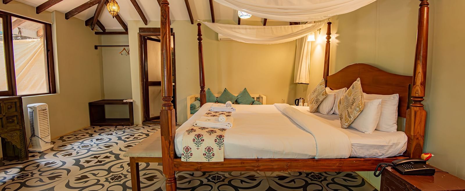 Side view of the spacious room with a large bed, bedside wooden table, and wooden-panelled ceiling at De Soul Santé, Morjim.
