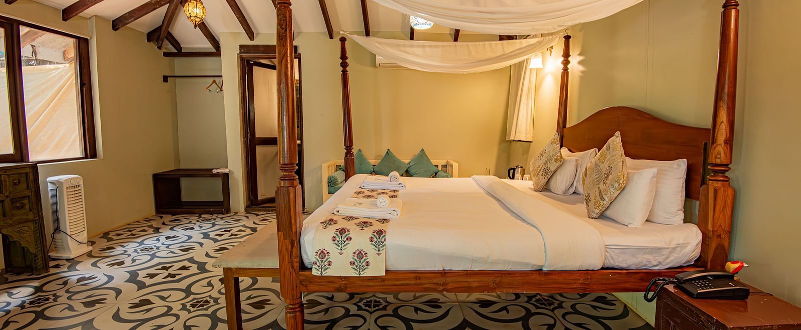 Side view of the spacious room with a large bed, bedside wooden table, and wooden-panelled ceiling at De Soul Santé, Morjim.
