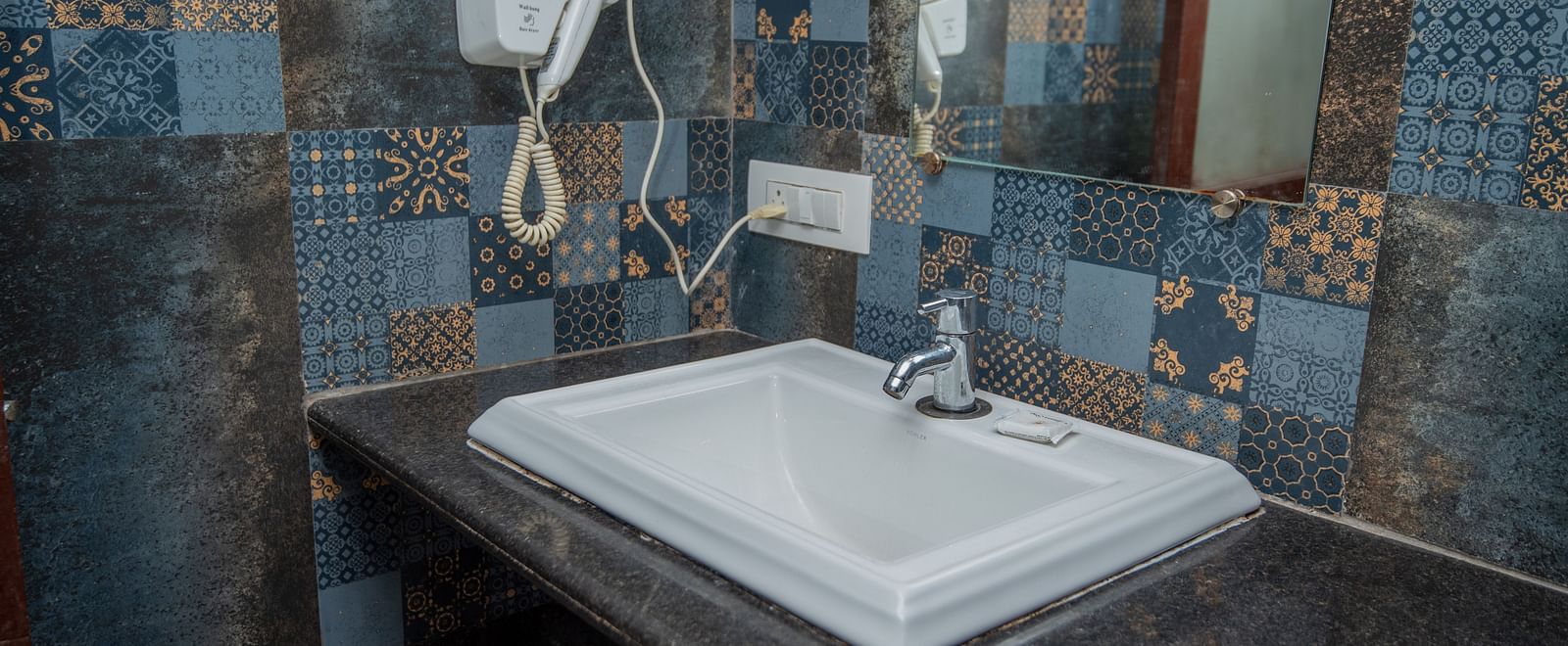 View of washbasin with a wall-mounted hair dryer and a wall-mounted mirror above it at De Soul Santé, Morjim.