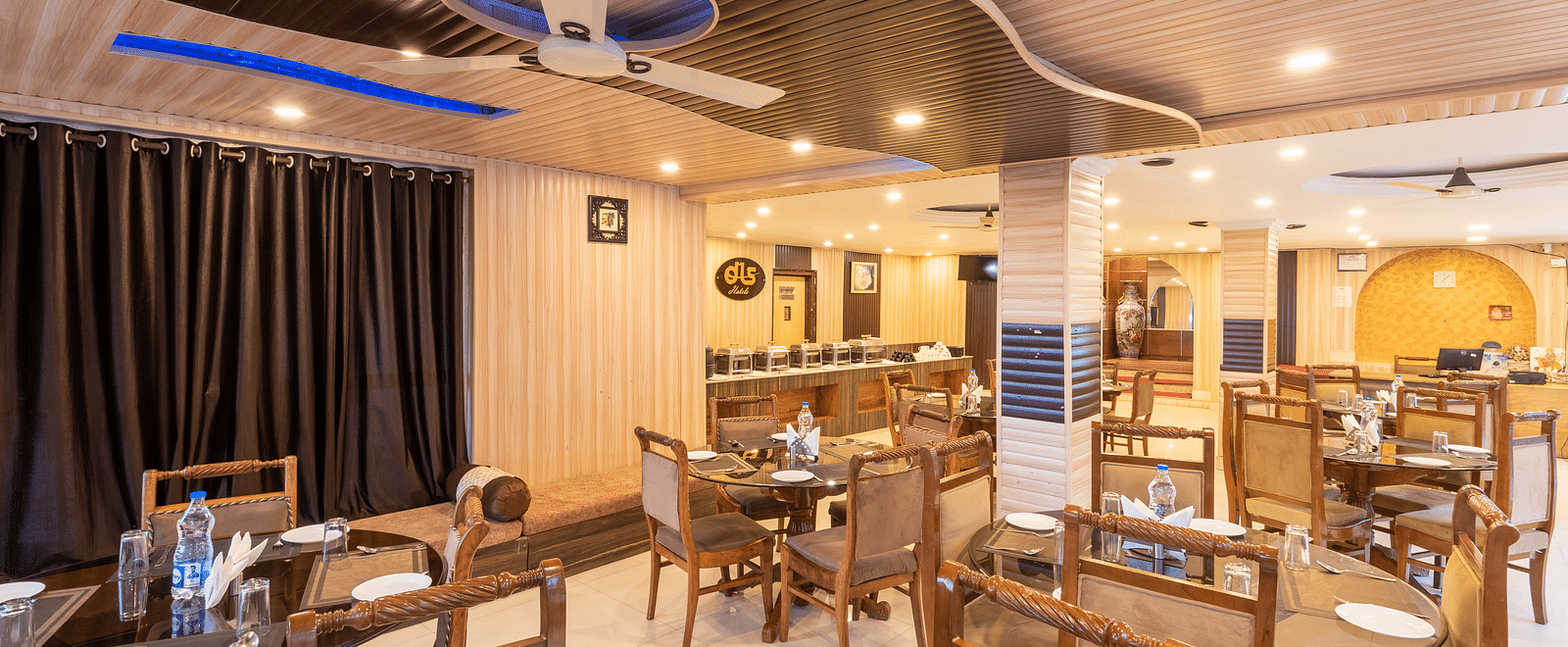 A dining area in Anupam Resort. The room features round tables with white tablecloths, wooden chairs, and dark curtains | DLS Anupam Resort, Dharamshala