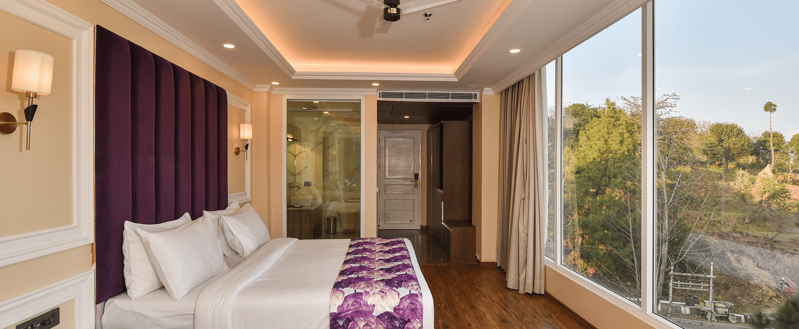  A well-designed bedroom with a comfortable bed, purple bedding, and large windows that open to views of the beautiful mountain landscape.