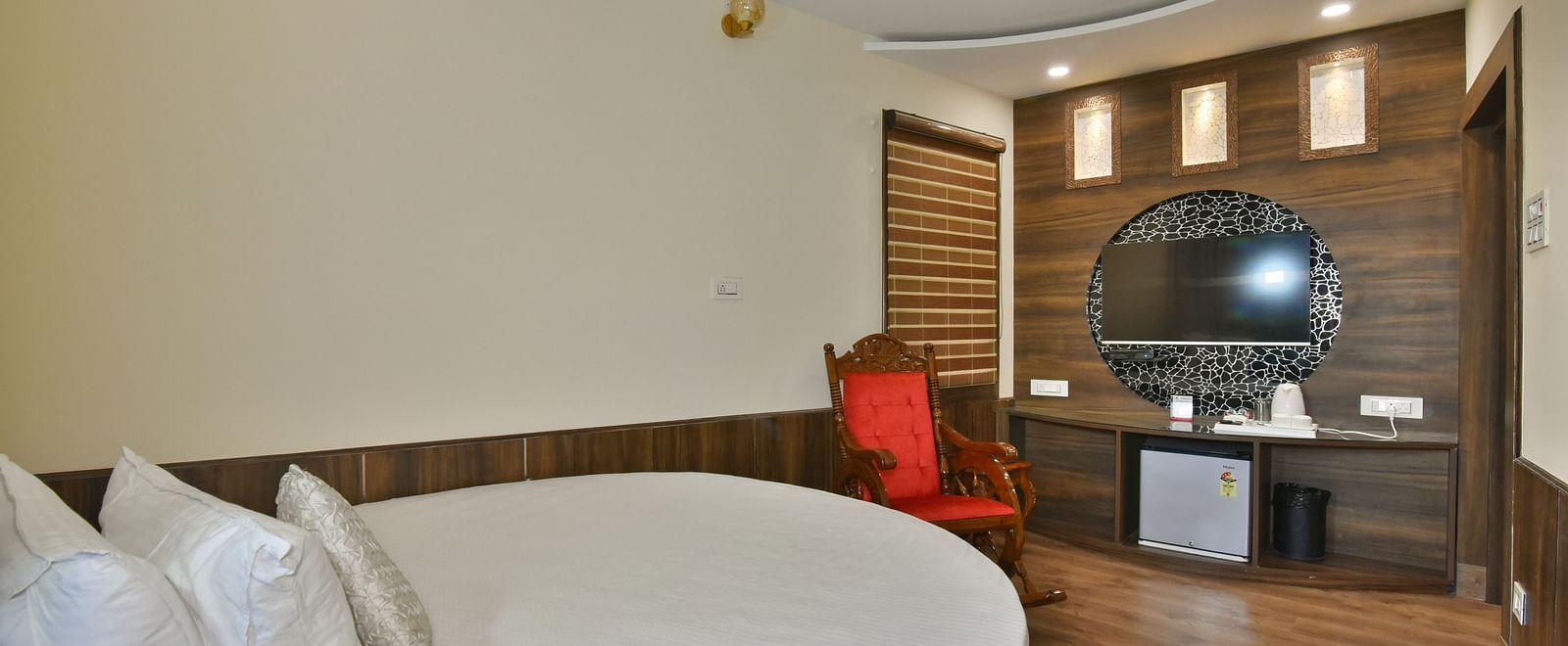 A Deluxe Room at DLS Dalhousie Valley Resort with a round  king size bed, mirror and a resting chair.