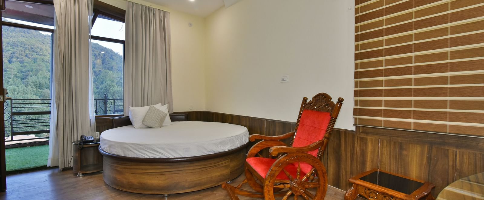 A Deluxe Room at DLS Dalhousie Valley Resort with a round king size bed, a chair and a balcony 