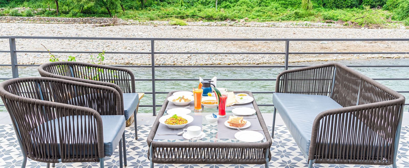 Various dishes plated and kept on the table of a restaurant at DLS Divine River Resort and Spa surrounded by lush greenery and river views.