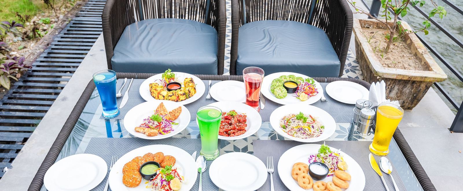 Various dishes plated and kept on the table of a restaurant at DLS Divine River Resort and Spa surrounded by lush greenery. 