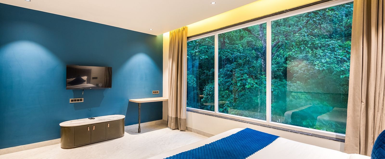 Deluxe Room at DLS Divine River Resort and  Spa featuring a  king bed, side table, TV and balcony with forest views.