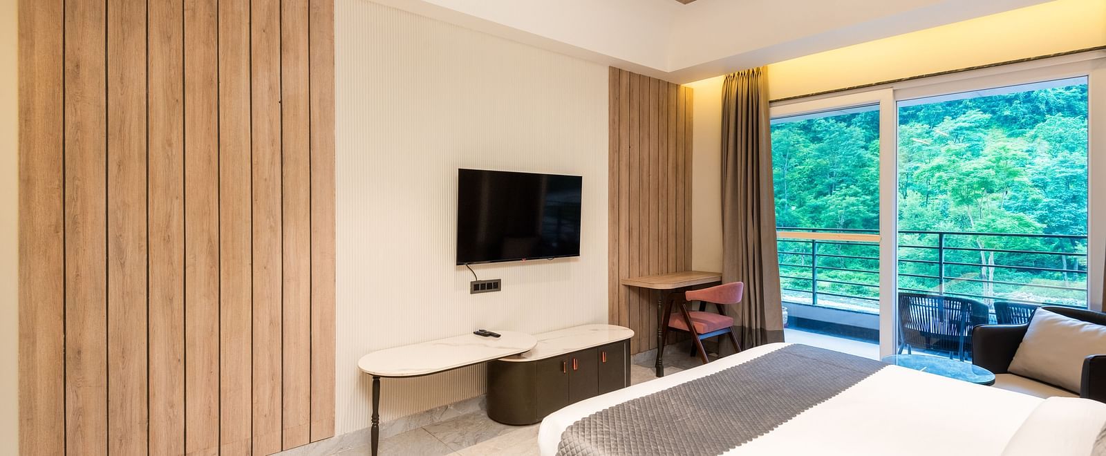 Deluxe Room at DLS Divine River Resort and  Spa featuring a  king bed , side table, TV and balcony with forest views.