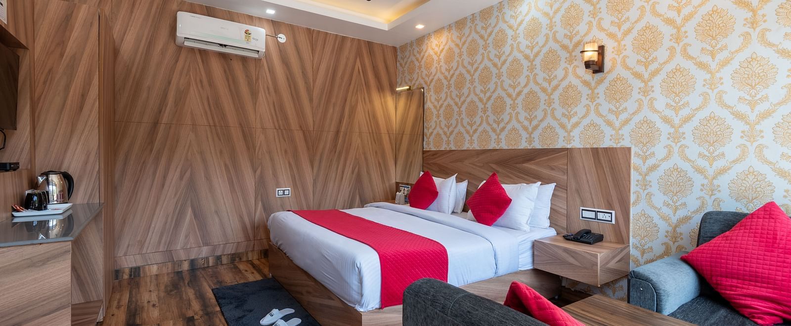Modern hotel room with wooden interiors, a double bed featuring red accents, stylish wallpaper, a sitting area, and an electric kettle station - DLS Nature Trinket Resort, Dalhousie.