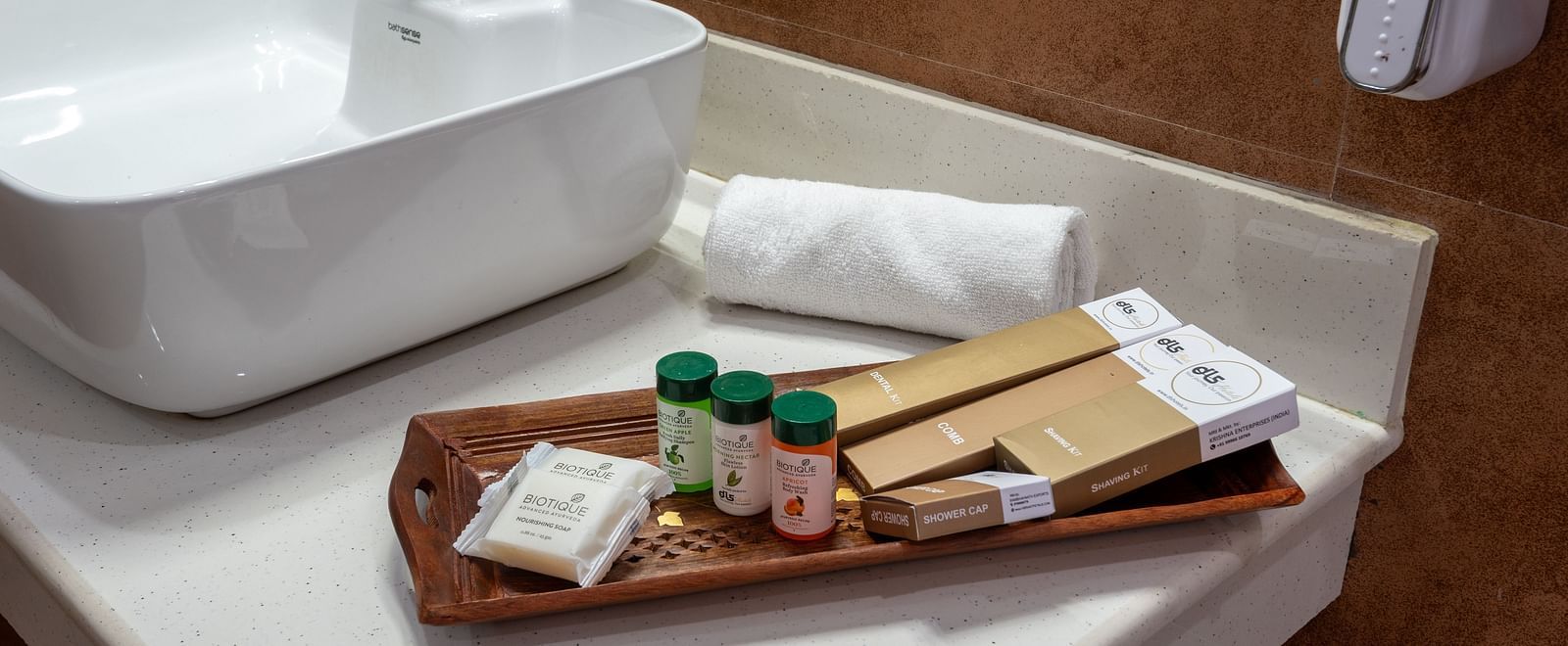  A close-up view of a bathroom sink with a modern white basin, a wall-mounted soap dispenser, and a tray holding toiletries such as small bottles, soap, and towels on a white countertop - DLS Nature Trinket Resort, Dalhousie.