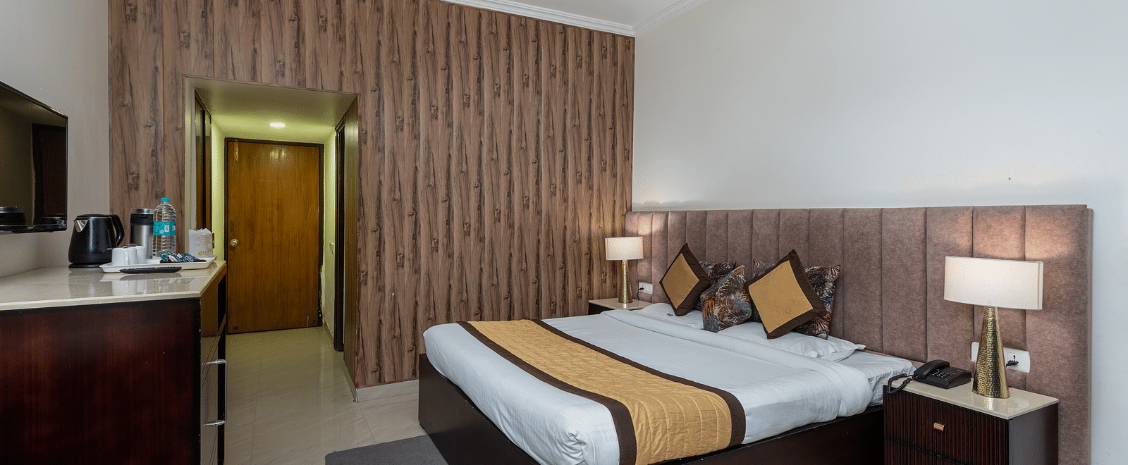 The image shows a hotel room with a large bed, two nightstands, a dresser, and a TV. There is also a door | DLS The Pearl