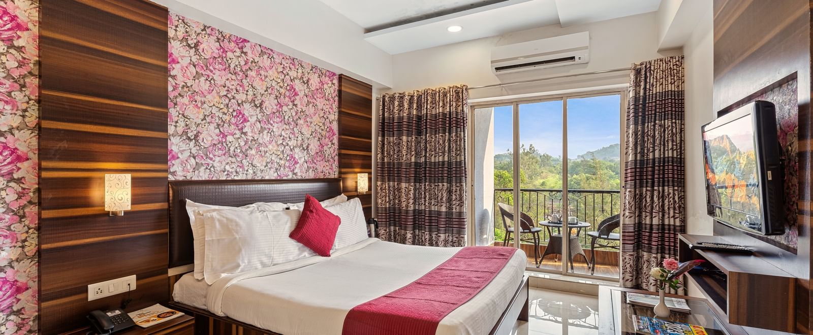Charming guest room at Mayur Retreat featuring floral wallpaper, pink accents, a balcony, and a TV setup.