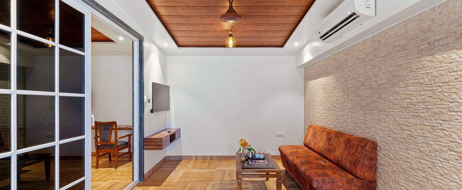 Sitting area at Mayur Retreat with a wooden bench and textured walls, adjoining a bedroom via glass sliding doors.
