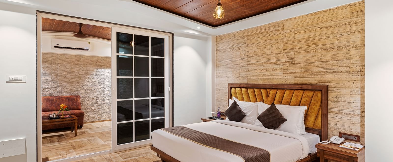 Cosy bedroom at Mayur Retreat featuring a double bed, wooden ceiling, warm lighting, and sliding glass doors opening to a balcony.