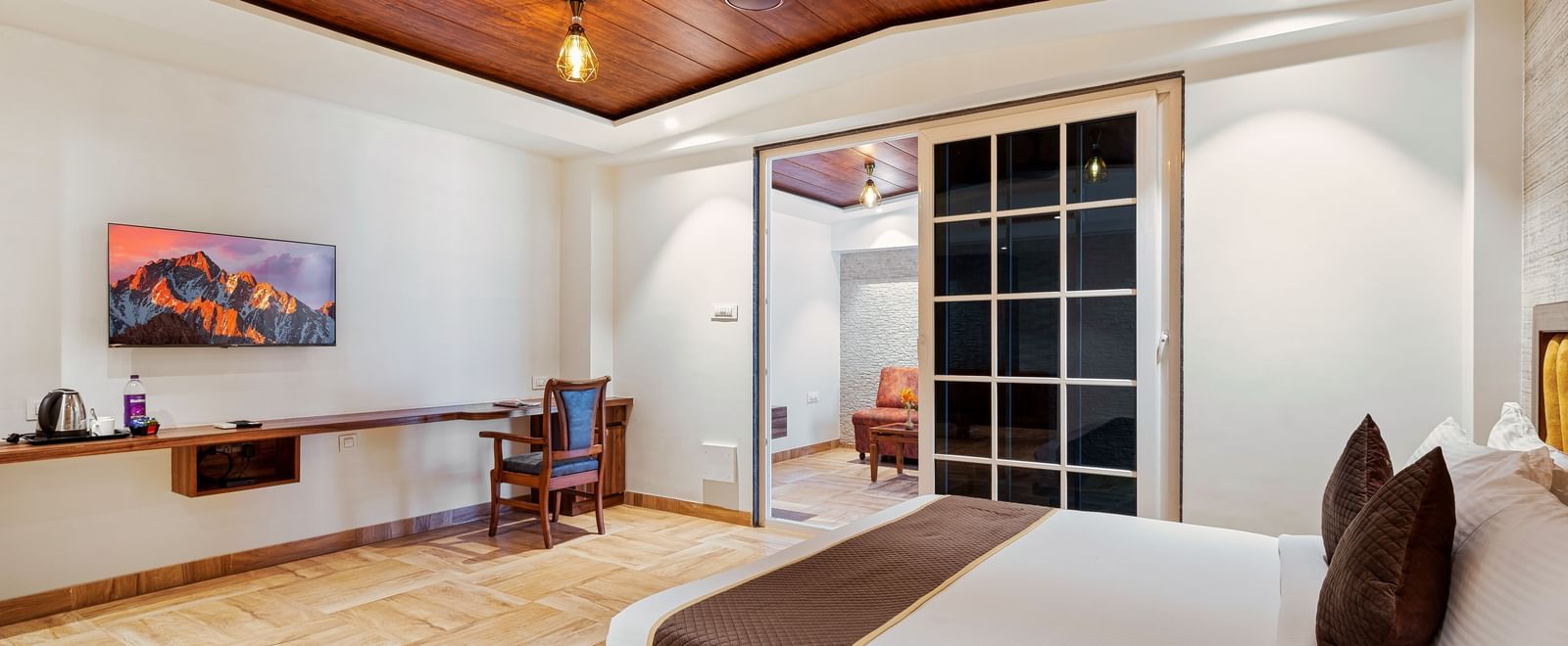 Spacious room at Mayur Retreat with a large bed, wall-mounted TV, and wood-accented ceiling, designed for comfort and relaxation.