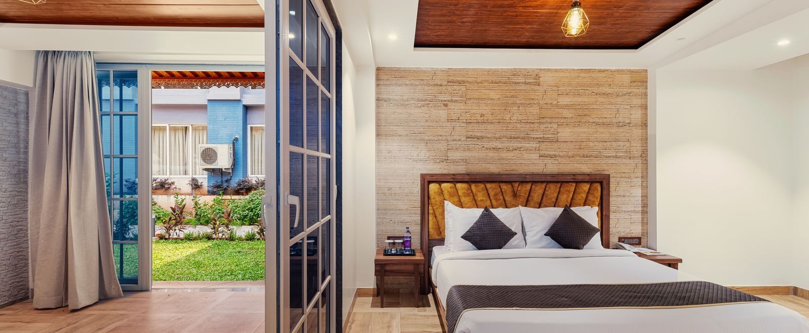 Bright bedroom at Mayur Retreat with a large bed, wooden flooring, and glass doors that open to a private patio.