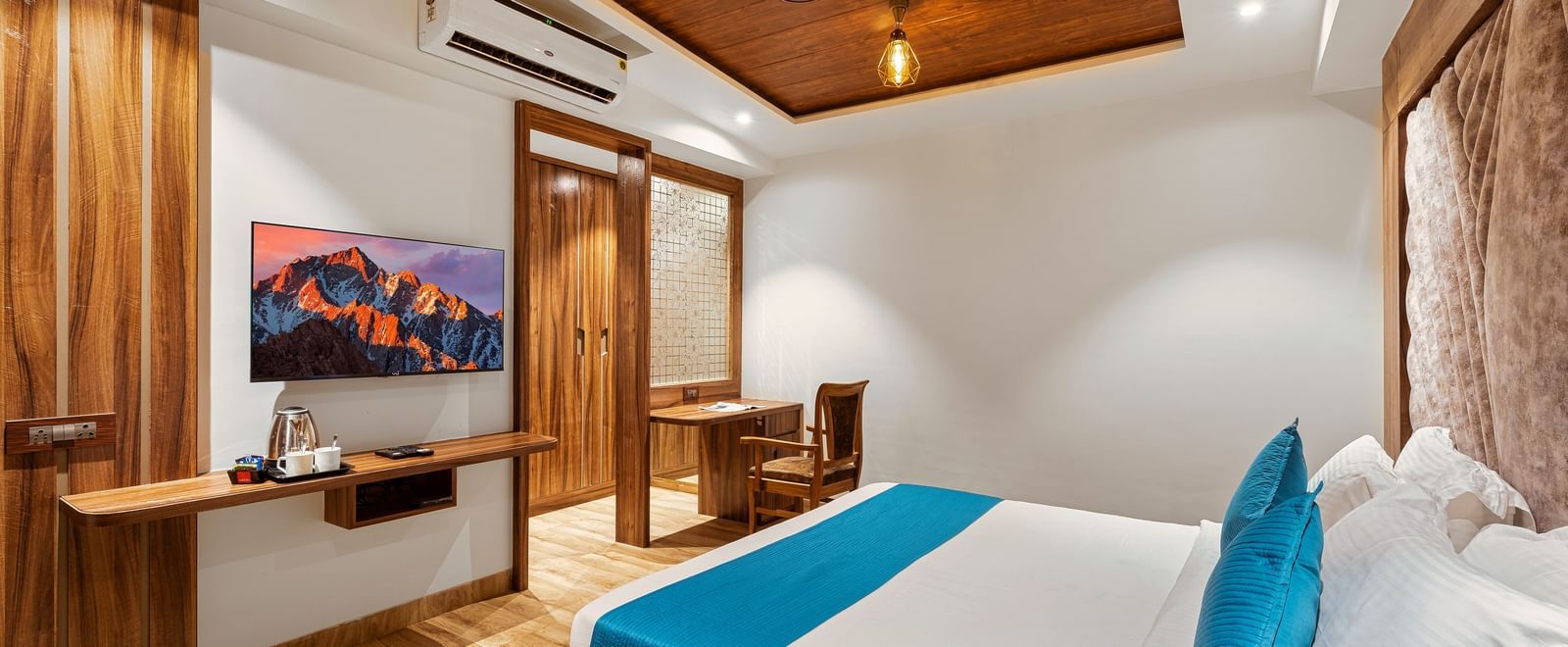 Well-lit bedroom with wooden furnishings, wall-mounted TV, and decorative artwork at Mayur Retreat.