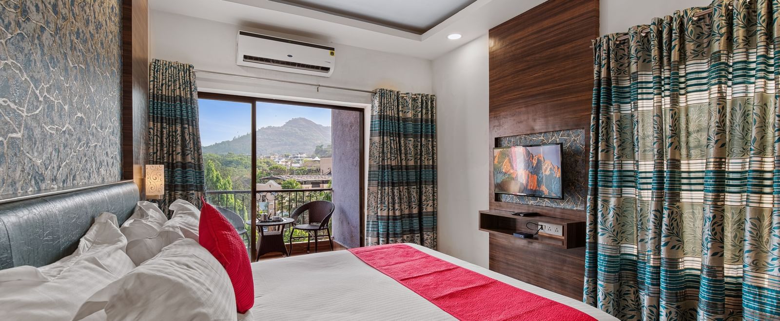 Spacious room at Mayur Retreat featuring twin beds with red throws, patterned curtains, and natural light.