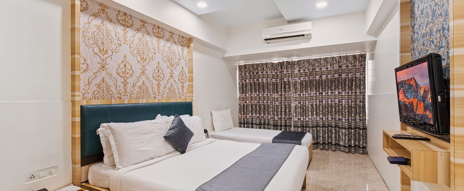 Modern hotel room with a king size bed and a singe bed at Mayur Retreat, contemporary lighting, and a flat-screen TV for a comfortable stay.