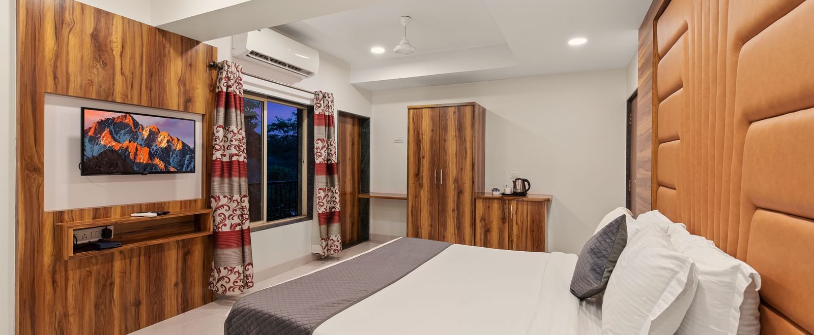 Comfortable guest room at Mayur Retreat with a white bed, cushioned headboard, and wall-mounted TV.