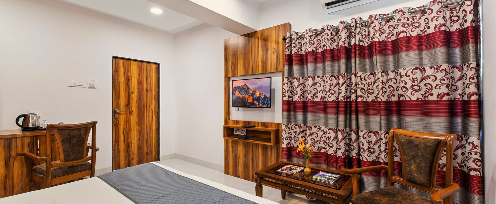 Traditional-style room at Mayur Retreat with wooden furniture, patterned curtains, and a grey bedspread.