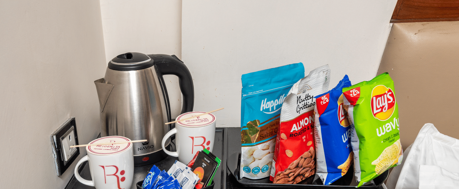 Tea and coffee maker with kettle, mugs, and snacks at DLS Hotels On The Ganges.