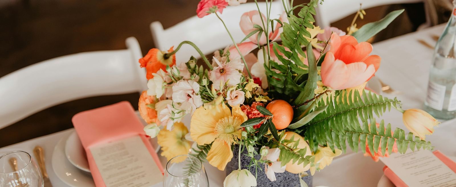 A vibrant floral centrepiece featuring an assortment of flowers, sits on a table set for an event.