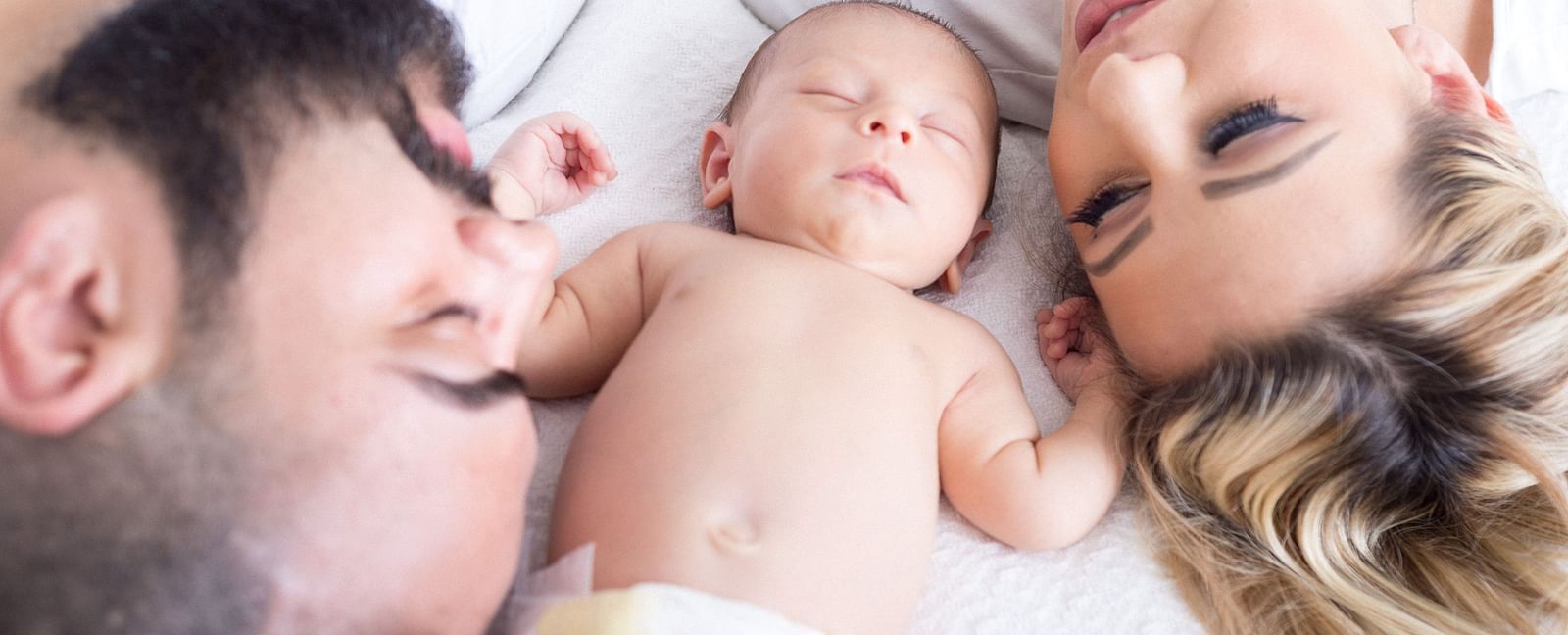 A close up shot of a couple sleeping with a toddler in between them. 