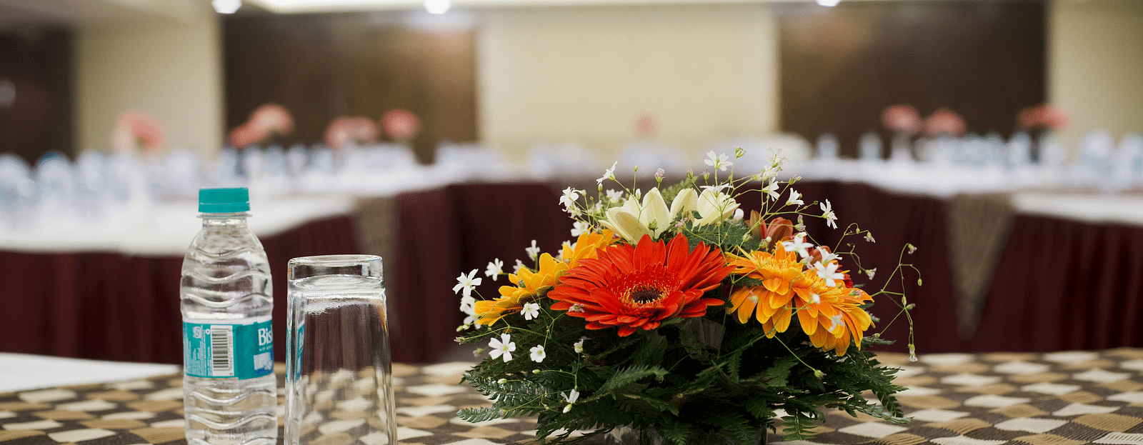 A conference room at The Manor, Bareilly, featuring a long wooden table with a centre piece of fresh flowers in a vase, neatly arranged alongside water bottle