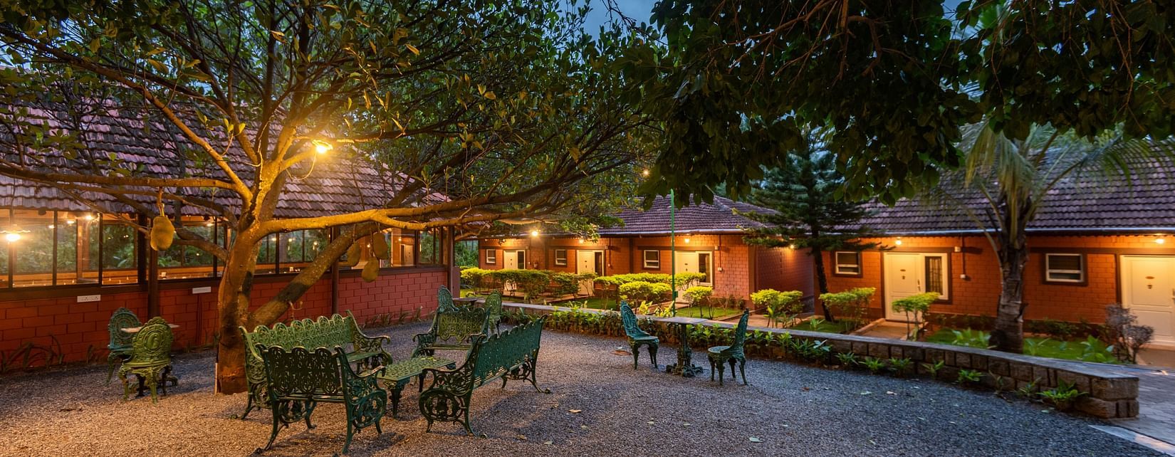 an open air lounge area with tree cover and rooms on the side  - Ibex River Resort, Pollachi
