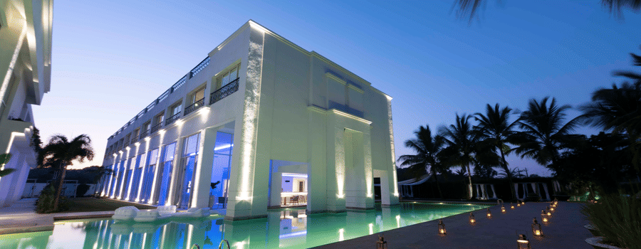  The Mansion House resort exterior at twilight with modern white columns, reflective pool, palm trees, lanterns, and blue-lit windows, creating a serene and luxurious evening atmosphere.