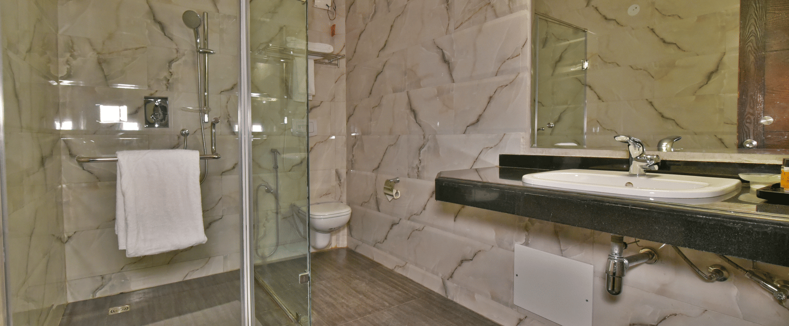 A shower cubicle with a wash basin beside it, featuring toiletries placed on the counter at DLS Hillcrest Resort, Shimla.