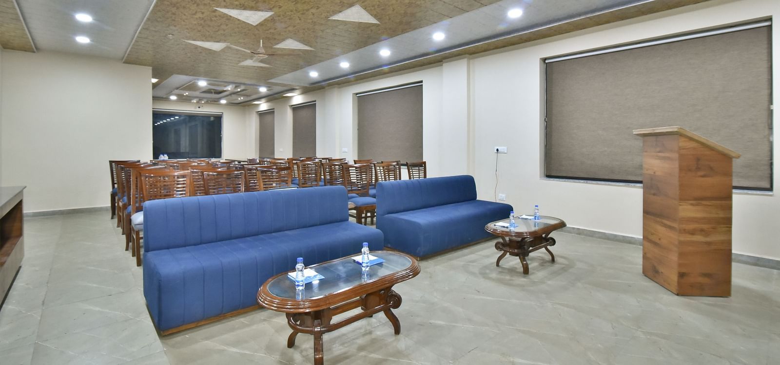 A banquet hall with a blue sofa and wooden chairs facing the podium at DLS Ark Holiday Inn, Banikhet.