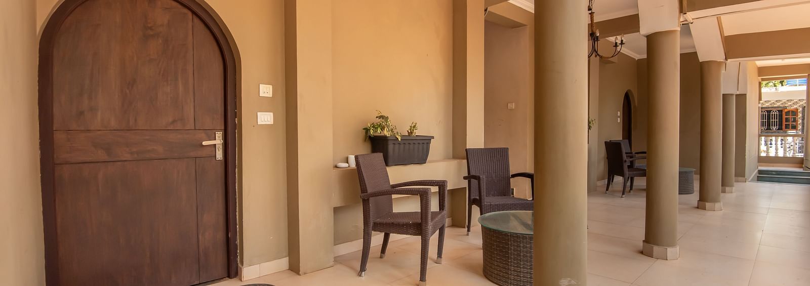 Arched wooden doorway leading to a spacious hallway with table, chairs, and warm lighting at De Soul Santé, Morjim.