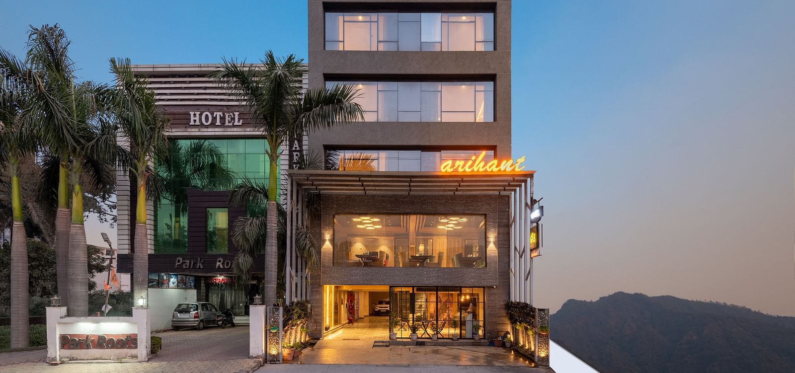 A facade image of DLS Hotel Arihant, Haridwar with trees in front and a mountain in the background