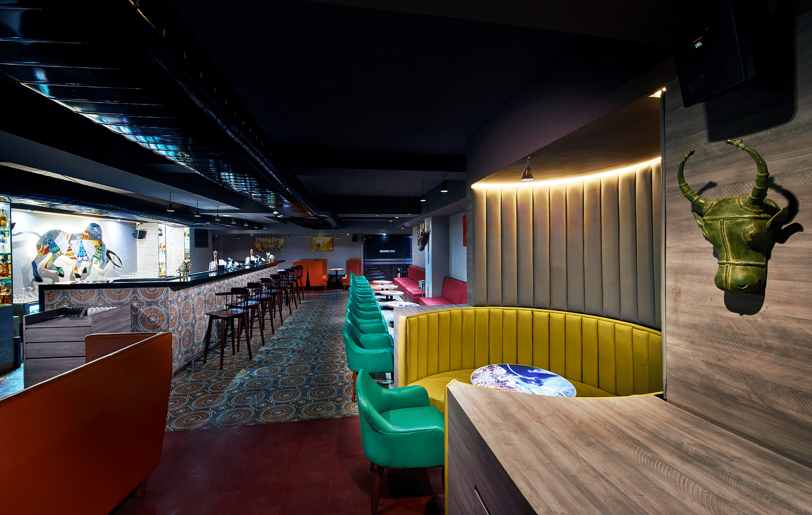 A brightly lit bar with red couches, a long bar counter, and a colorful wall mural | Regency Tirunelveli By GRT Hotels