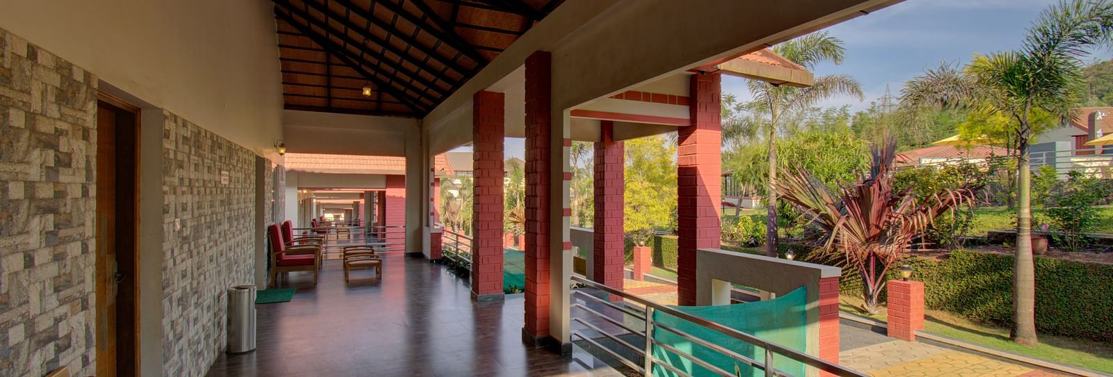 A tiled balcony with chairs that overlooks the main passage and greenery | Woodstock Resorts, Coorg
