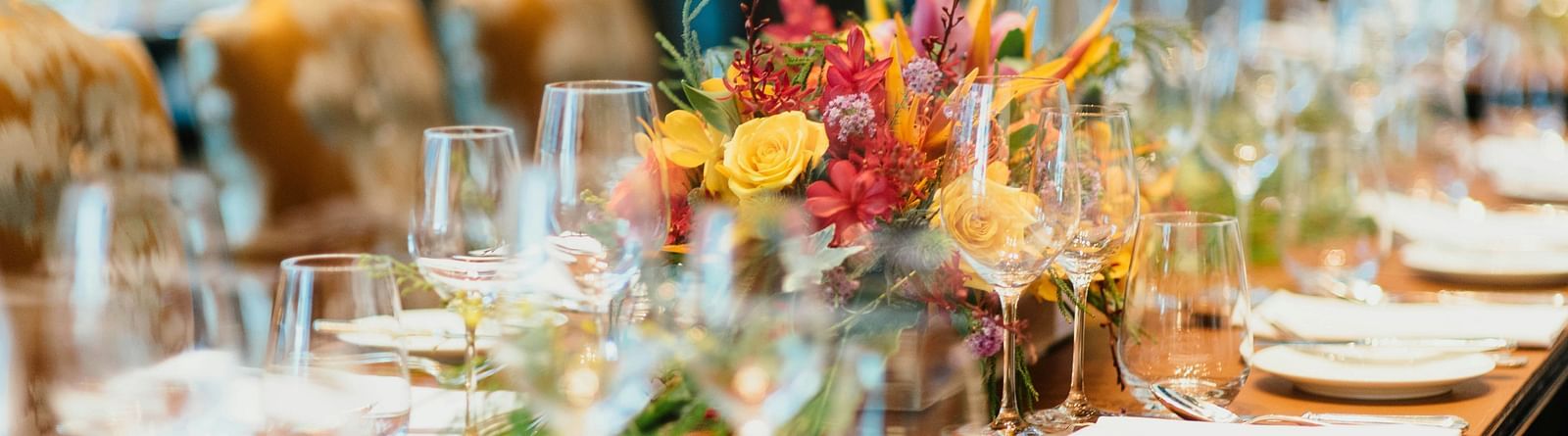 Elegant dining table set for a formal event with floral centrepieces and wine glasses.