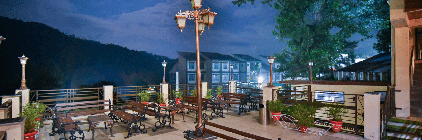 Side view of open terrace at DLS Dalhousie Valley Resort featuring benches and tables during evening.